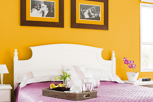 Quarto de casal com parede da cama em amarelo forte e lençois rosas
